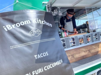 iBroom Kitchenの看板の奥、男性がキッチンカー内で調理をしている様子の写真