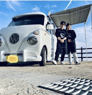 白いワゴン車の横に立つエプロンを付けた男性と女性の写真