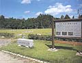 木々に囲まれた広場の入り口に石銘板と看板が設置されている水池土器製作遺跡の写真