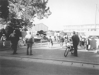 明星小学校の校門に立って防犯活動をしている保護者の写真