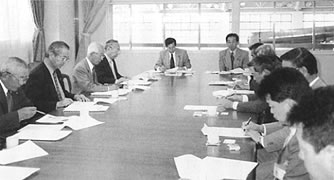 会議用のテーブルに向かい合って席につき話を聞いている委員の写真