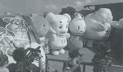 横一列に並んだ4体のゆるキャラを見ている観客の後ろ姿の白黒写真