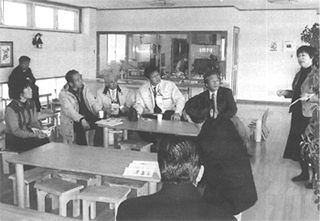 立って話をしている女性と椅子に座って話を聞いている視察委員の写真