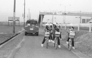一台の車の横を通り過ぎた自転車通学をしている子供たちの写真