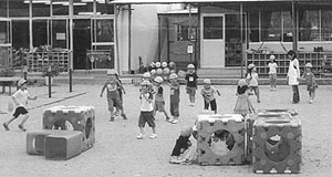 四角いトンネルの遊具が置いてある園庭で遊んでいるみどり保育所の子供たちの写真