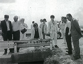 議員の方々がガードレールの下の用水路を覗き込んで見ている白黒写真