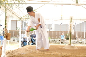 お酒が入った一升瓶を持った行司が土俵に撒いている写真