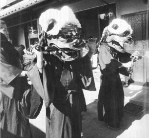 袴を着て獅子舞の被り物を被った2名が民家の玄関先に立っている坂本の獅子舞について書かれた広報めいわ第159号（昭和56年）掲載記事の写真