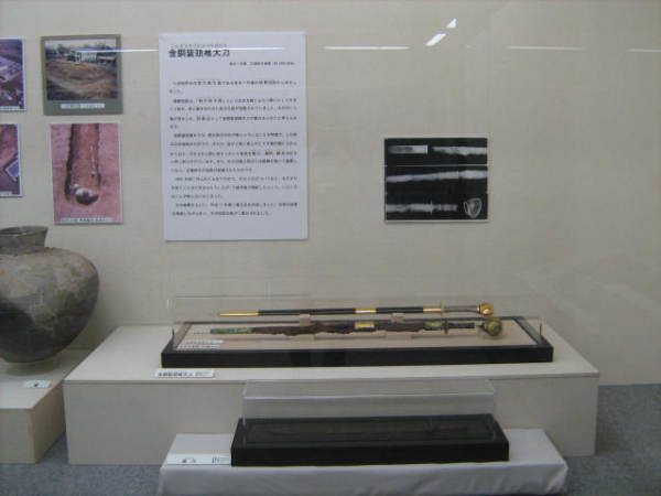 後方の壁に説明資料や写真が貼られ、手前に2本の刀が展示されている写真