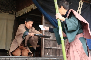 男性がお盆に乗せた熨斗袋を紋付袴を着た男性に渡している写真
