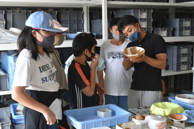 粘土を使って再生された土器を先生が両手で持って、観察しており、周りにいる生徒も興味深く見ている様子の写真