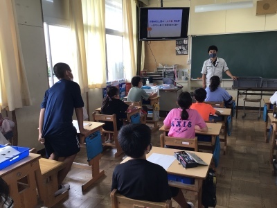 生徒の皆さんが自席に座っている教室で、職員の男性が教卓の横に立ち、一人の男子生徒が発表をしている授業風景の写真