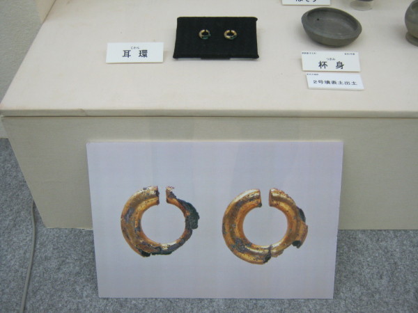 展示台に2つの耳環が並んで置かれ、手前に拡大した耳環のボードが立てかけられている写真