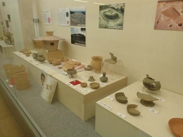 壁に発掘時の写真などが貼られ、手前に壺や杯、埴輪などが展示されている写真