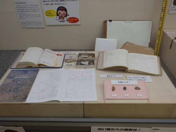 展示台の上に地図や書籍が開いて置かれ、3つの小さな石器が置かれた石器クイズと書かれたスペースが置かれている写真