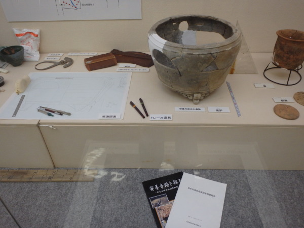 展示台の上に図面やトレース道具、発掘されつなぎ合わせた大きな香炉が展示されている写真