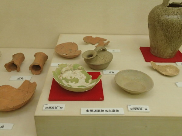 「金剛坂遺跡出土遺物」と書かれた展示台に置かれた陶器椀や壺をアップで撮影した写真