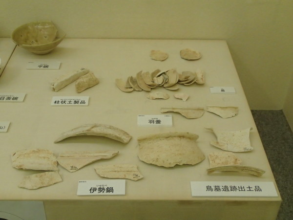 「鳥墓遺跡出土品」と書かれた展示台に羽釜や伊勢鍋と書かれた欠片などが展示されている写真写真