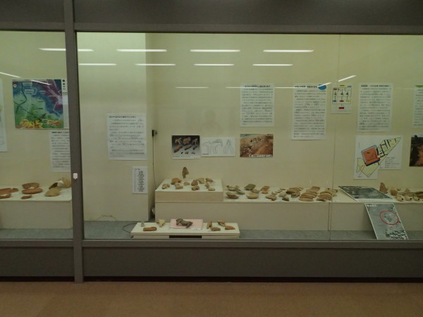 後方の壁に発掘場所や遺跡の写真、資料が展示され手前に土馬や遺跡の欠片などが展示されている写真