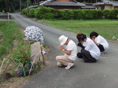 3名の女性が集落の入り口に祀った山の神様に拝んでいる様子の写真