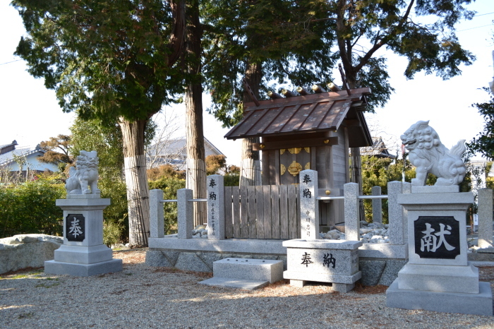 樹木が生えている手前左右に石造りの狛犬が設置され中央に小さな祠のある粟須美神社の写真