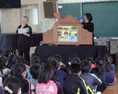 大型紙芝居が行われており、たくさんの児童の皆さんが座って興味深く見ている様子の写真