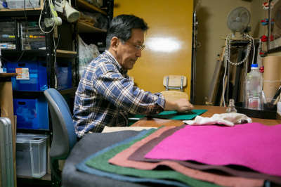 色とりどりの擬革紙が重なった奥で製造している男性の写真