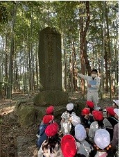 石碑前で生徒の皆さんが職員の男性の説明を聞いている写真