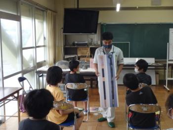 職員の男性が出土した剣の写真を子どもたちに見せて回っている授業風景の写真