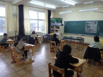生徒の皆さんが教室の自席につき、前方にあるモニターに写し出された映像を興味深く見ている様子を後方より写した写真