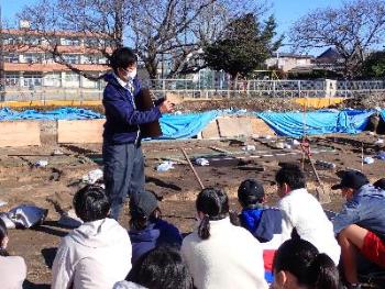 発掘現場で生徒の皆さんが説明を聞いている写真