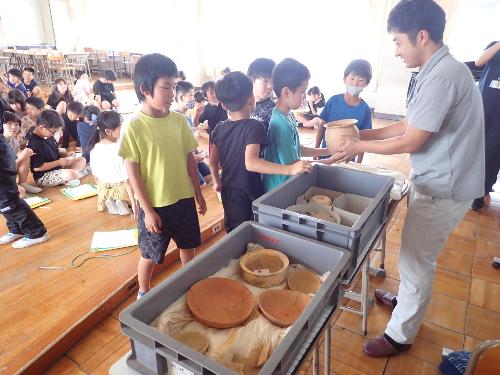 職員の男性が出土した土器を見せている写真