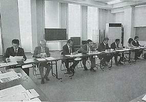 左側に横一列に設置された長机の席に議員の方々が座っている会議の様子の白黒写真