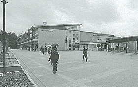 2階建ての大安中学校の校舎の手前の広場を歩いている人達の後ろ姿の白黒写真
