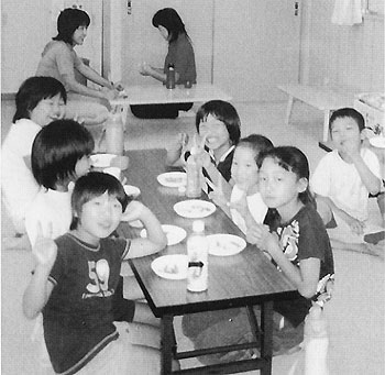ひとつのテーブルに集まっておやつを食べている上御糸児童クラブの子供たちの写真