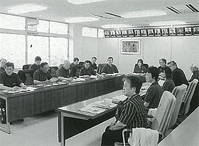 コの字に設置された長机の席に座っている参加者が話し合っている白黒写真