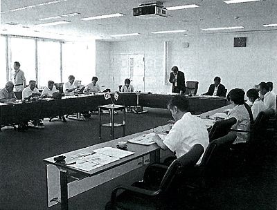 コの字型に設置されたテーブルに置かれた資料を見ながら話し合いをしている委員の写真
