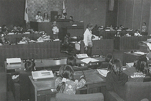 見学に訪れた小学生の子ども達が議会の席に座っている様子の白黒写真
