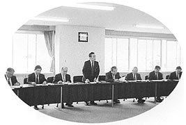 長机の席についている委員のうち、中央の1人の男性が席を立っている写真