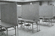 パイプ椅子が2脚ずつセットされた長机が4列並んでいる多目的室の白黒写真