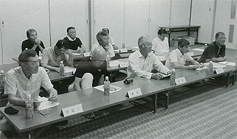 長机を3列に並べた席に議員の方々が座っている会議の様子の白黒写真