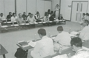 コの字に設置された長机の前に座っている説明会の参加者の白黒写真