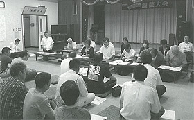 2列に設置された長机の席に座っている議員の方々と住民の方々が向かい合って座っている議会報告会の様子の白黒写真
