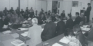 手前の長机の席に議員の方々が座り、奥に住民の方々が向かい合って座っている会議の様子の白黒写真