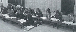 2列に並んだ長机の席に座っている参加者の白黒写真