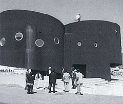 丸窓が設置された2つの円柱の津波防災ステーションの建物の前で関係者が集まっている白黒写真