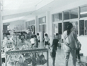 帽子や服がかけられた広い廊下で小さな子供たちが先生と一緒に遊んでいる白黒写真