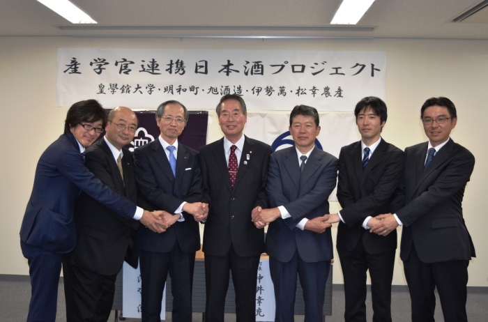 産学官連携日本酒プロジェクトと書かれた横断幕の前で、中井町長と関係者の方々７名が横一列に並び交差して握手し、記念撮影をしている写真