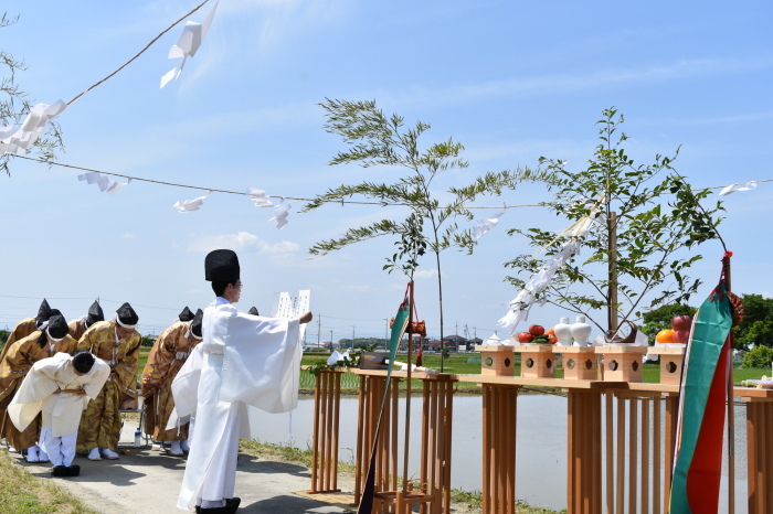 水の張った水田の前に、祭壇が設けられ、装束を着て整列した方がお辞儀をする中、神事が行われている様子の写真