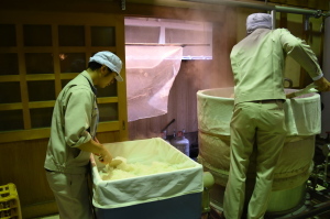蒸しあがった酒米を樽から大きなバットに出す作業をしている様子の写真
